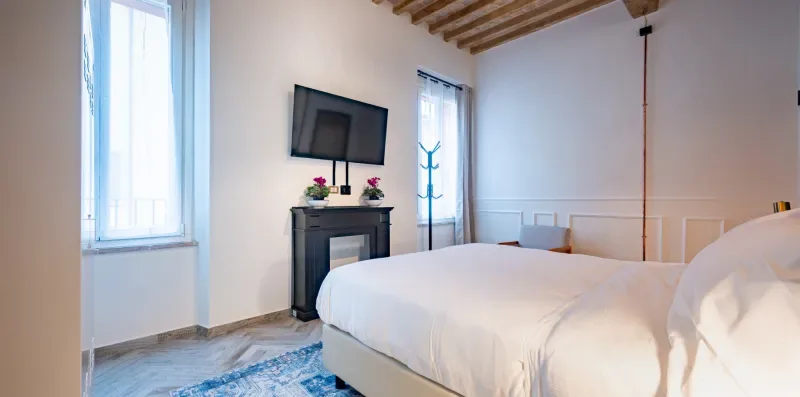 Un dormitorio con una cama grande, un televisor y dos ventanas altas.