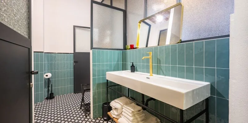 Un baño con azulejos, un lavabo blanco alargado y un grifo dorado.