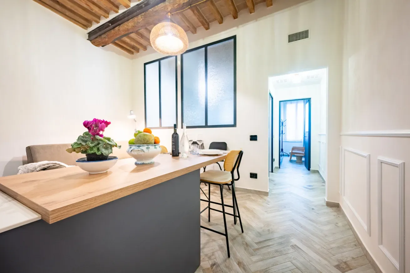 Un comedor luminoso tiene una mesa de madera, asientos y vigas de techo a la vista.