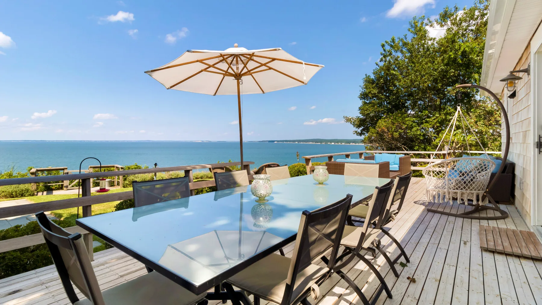 Una terraza junto al mar tiene una mesa de comedor bajo una sombrilla grande.