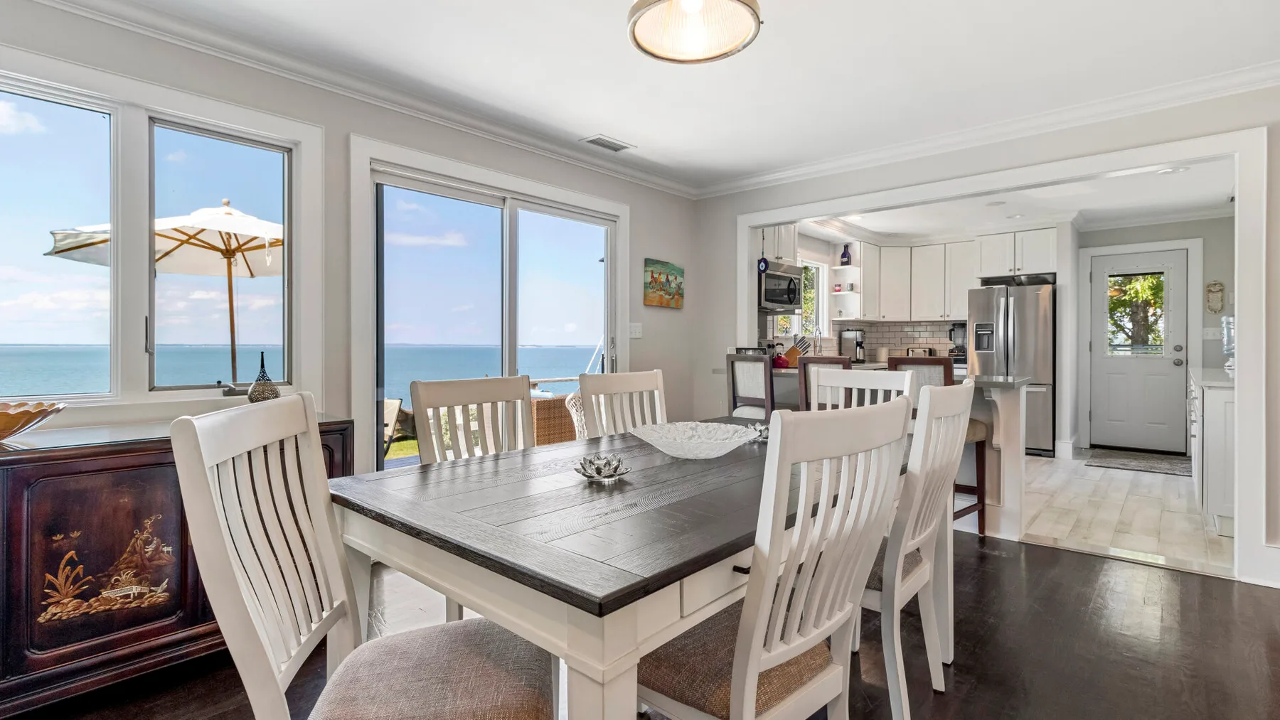 Comedor con mesa y sillas junto a grandes ventanales con vistas al mar.