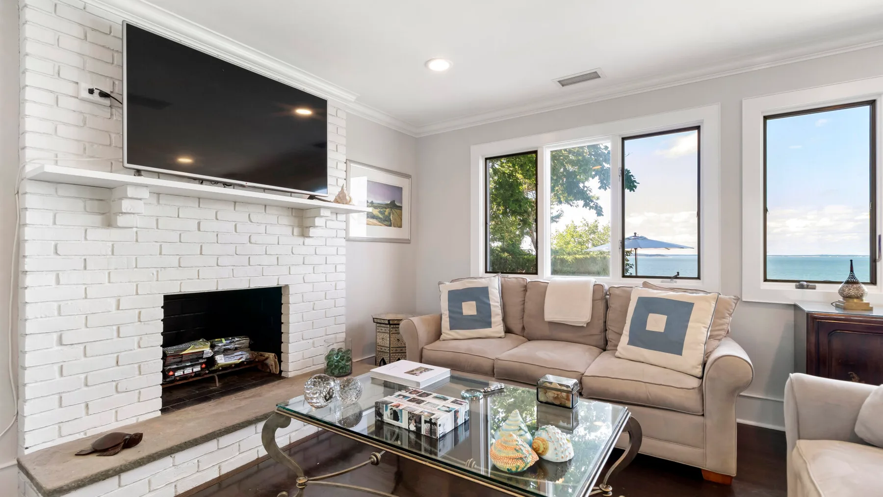 A bright living room with a beige sofa, glass coffee table, and large windows.
