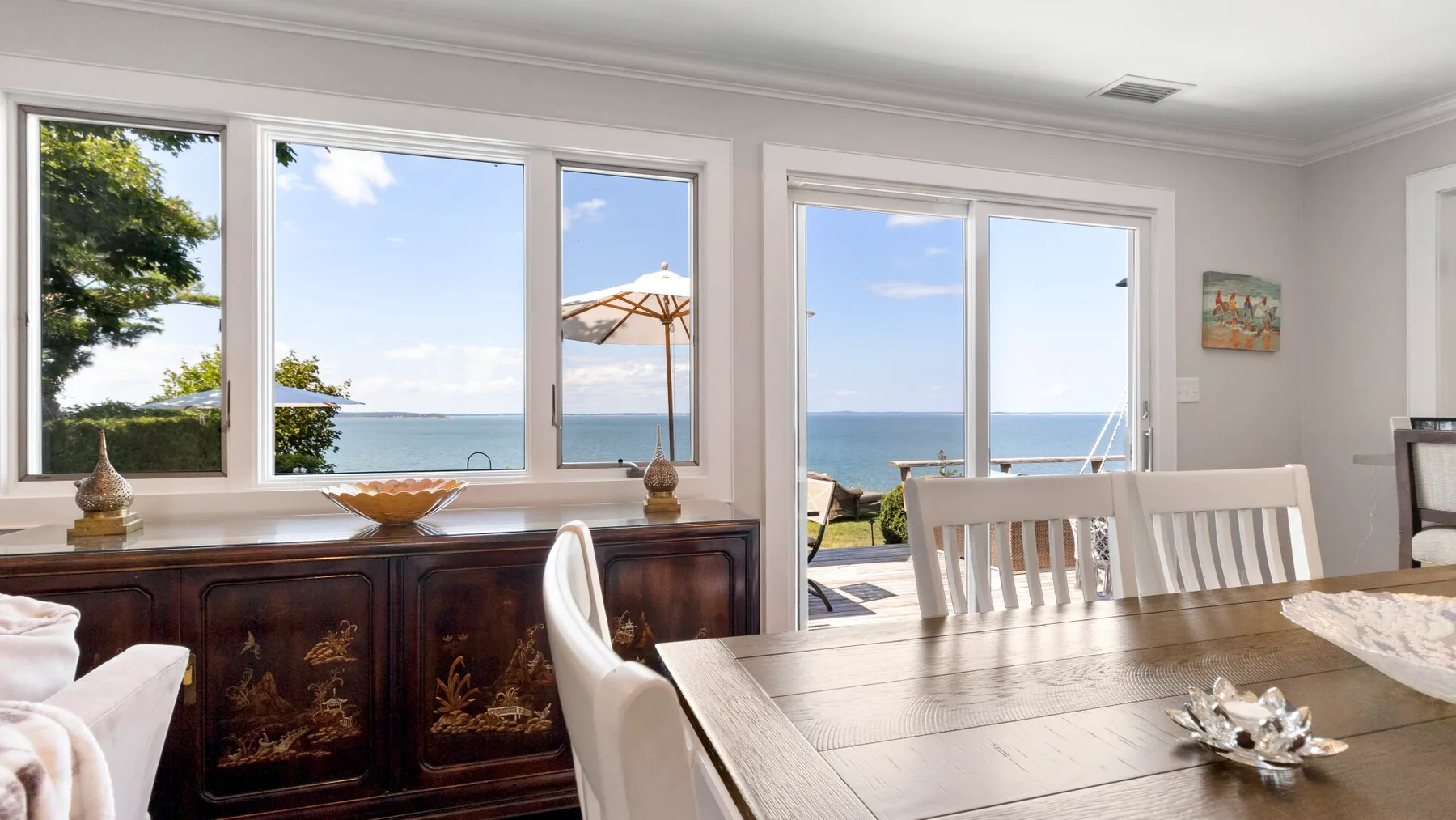 Comedor con una mesa de madera junto a grandes ventanales con vistas al agua.