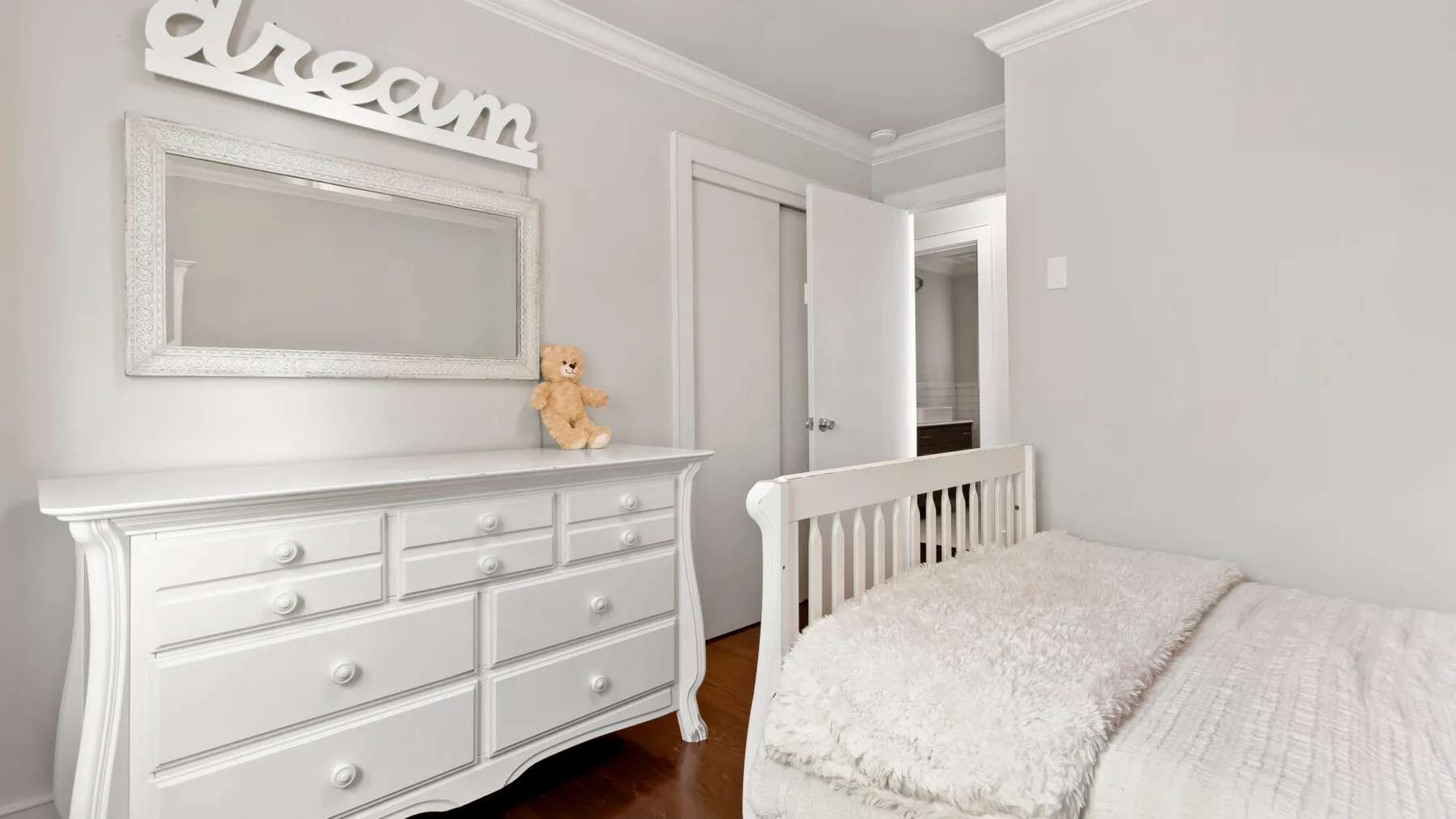 Un dormitorio luminoso con una cómoda blanca y una cama cubierta con ropa de cama clara.