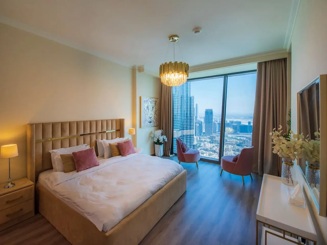 A bedroom with a large bed and floor-to-ceiling windows overlooking city buildings.
