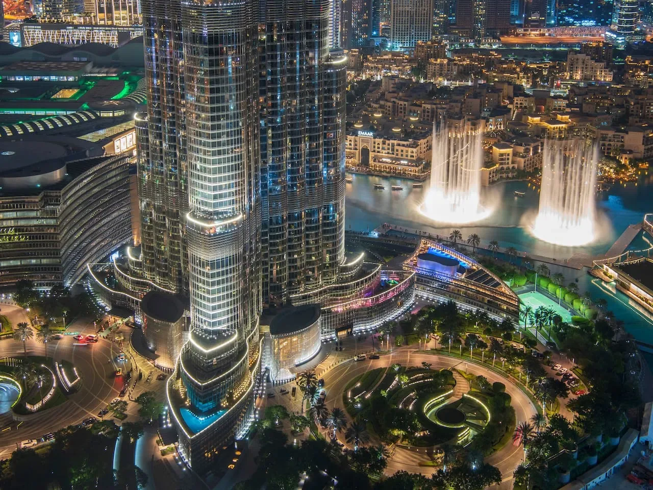 Nighttime cityscape with illuminated fountains and surrounding high-rise buildings.