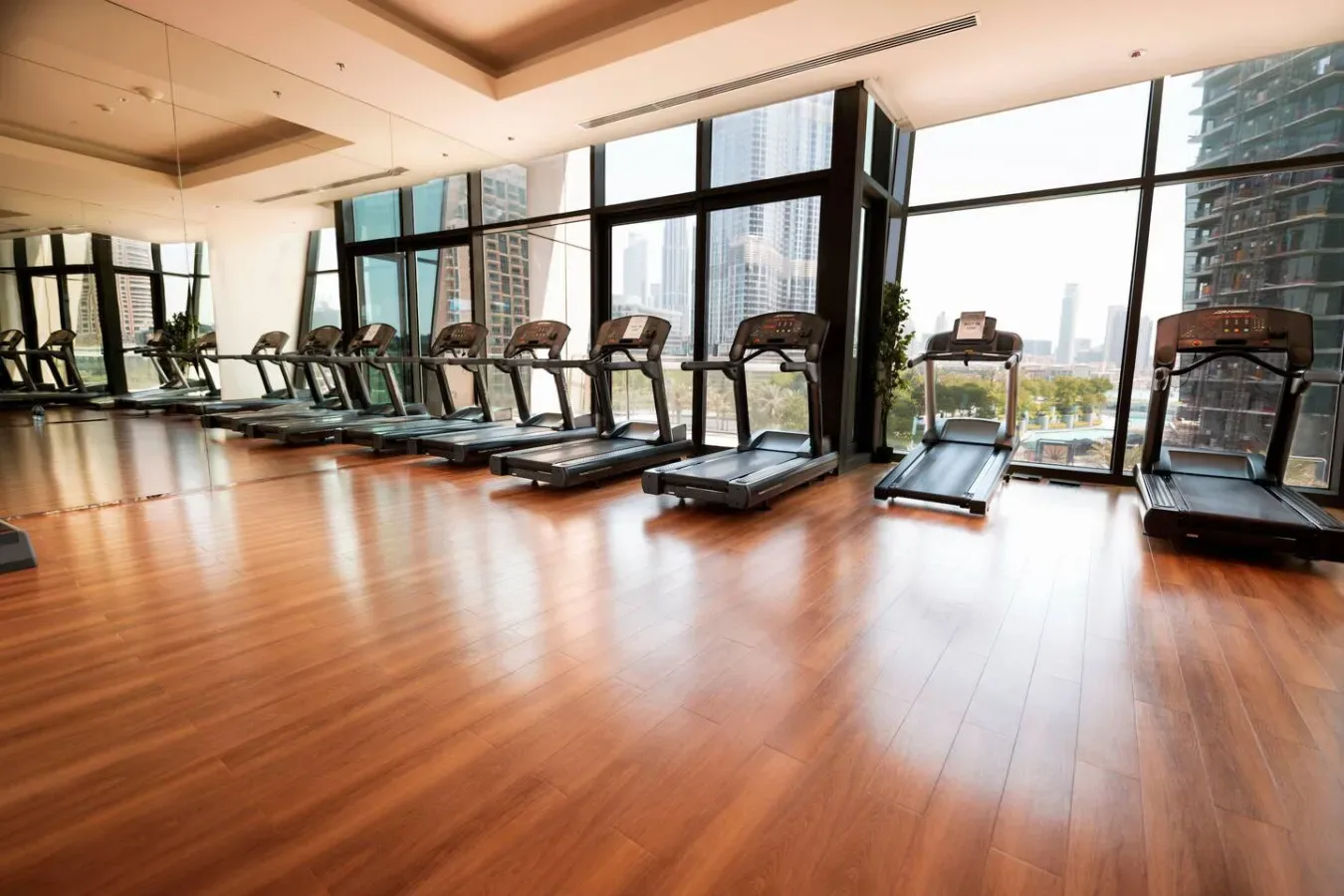 A gym with treadmills arranged beside large windows.