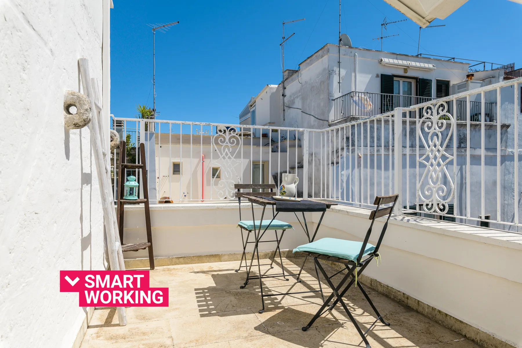 A sunny rooftop terrace with outdoor seating and white railings.
