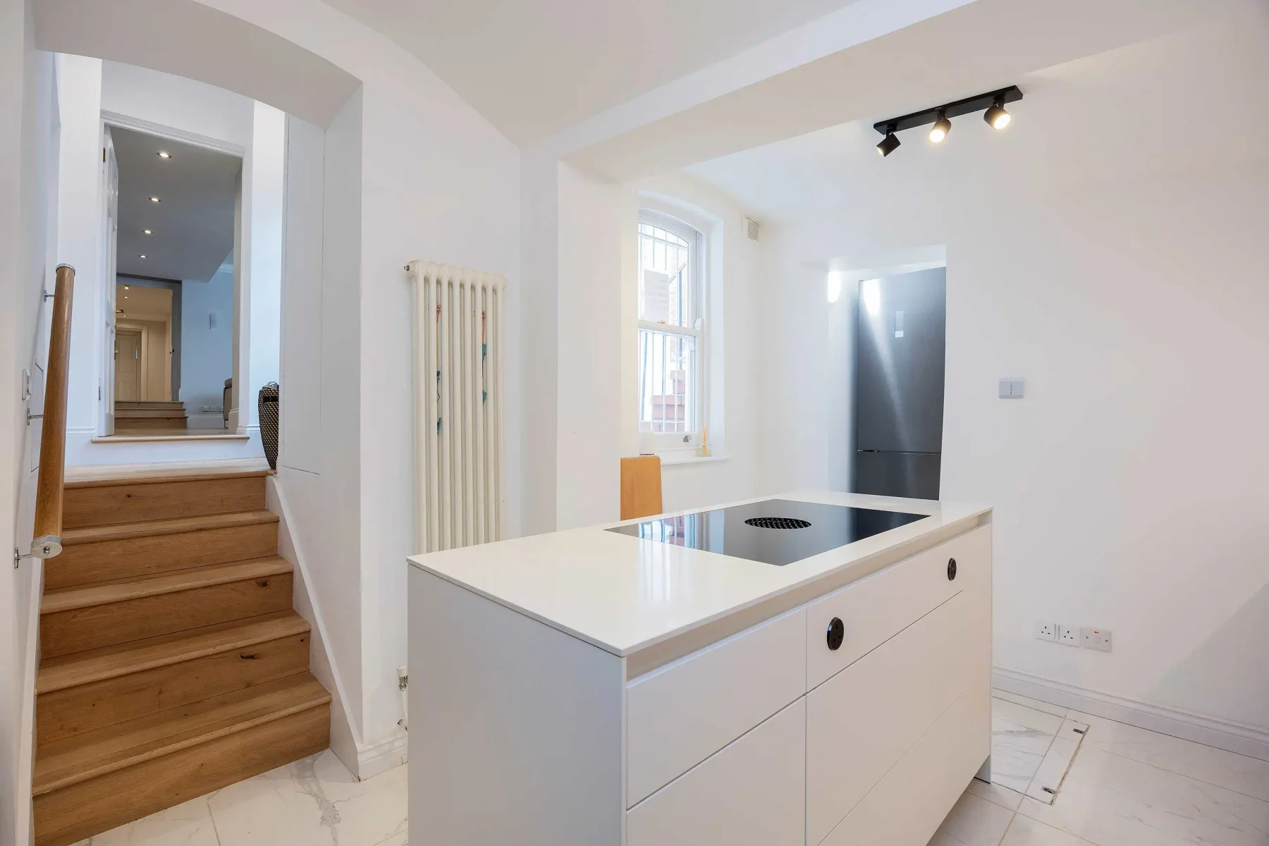 Una cocina luminosa con una isla blanca y escaleras de madera hacia otra estancia.