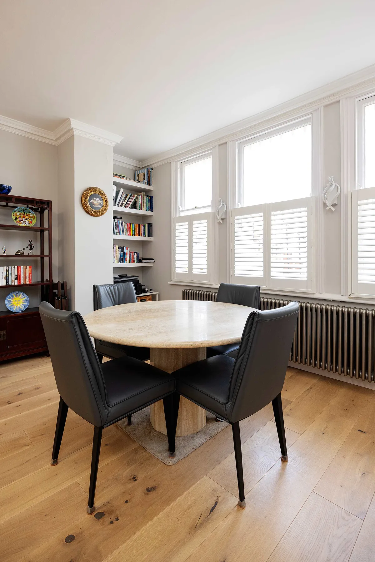 Comedor con una mesa de madera y sillas oscuras junto a ventanas altas.