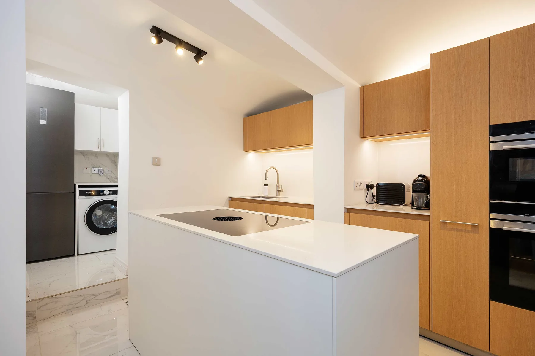 Una cocina moderna con isla blanca, fregadero y armarios de madera.