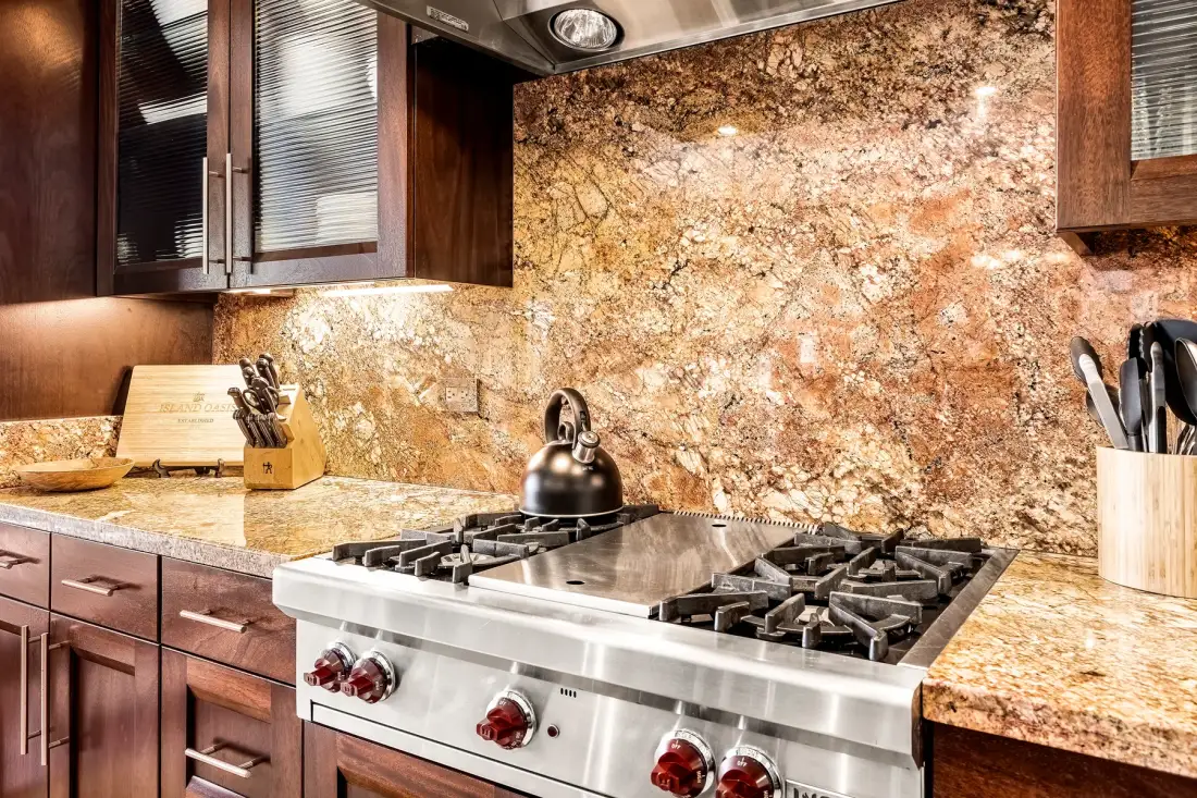 Una cocina con una estufa de acero inoxidable frente a un salpicadero de piedra moteada.