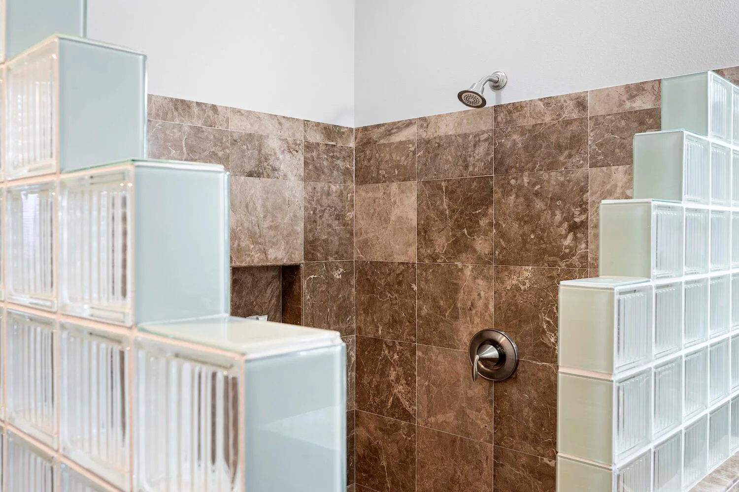 Una zona de ducha de baño con paredes de azulejos marrones y divisiones de bloques de vidrio.
