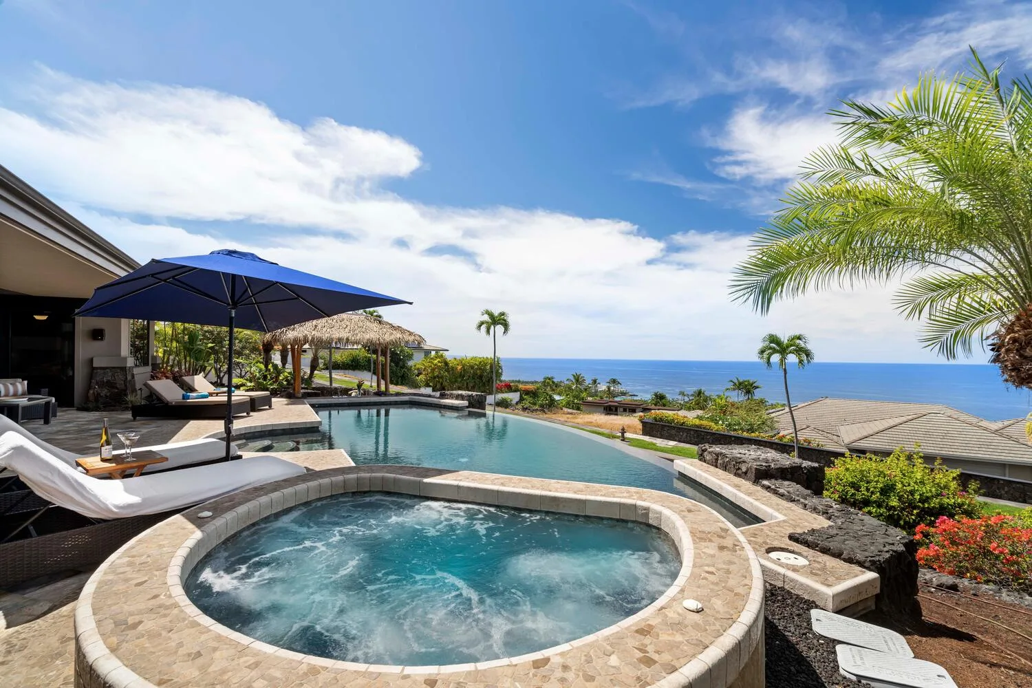 Una piscina al aire libre y un jacuzzi circular miran al océano bajo un cielo soleado.