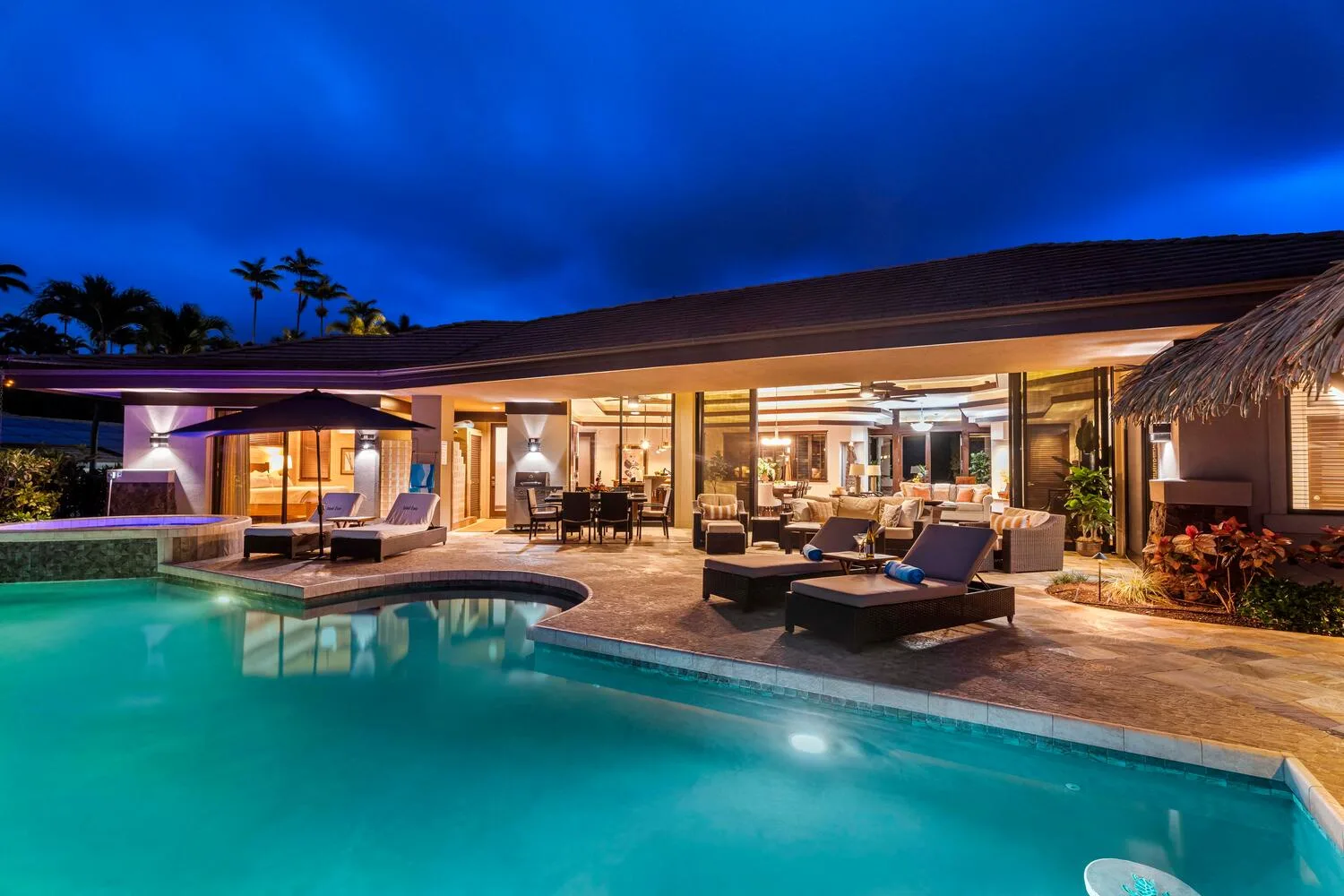 Una casa moderna iluminada da a una piscina y una zona de estar al aire libre al anochecer.
