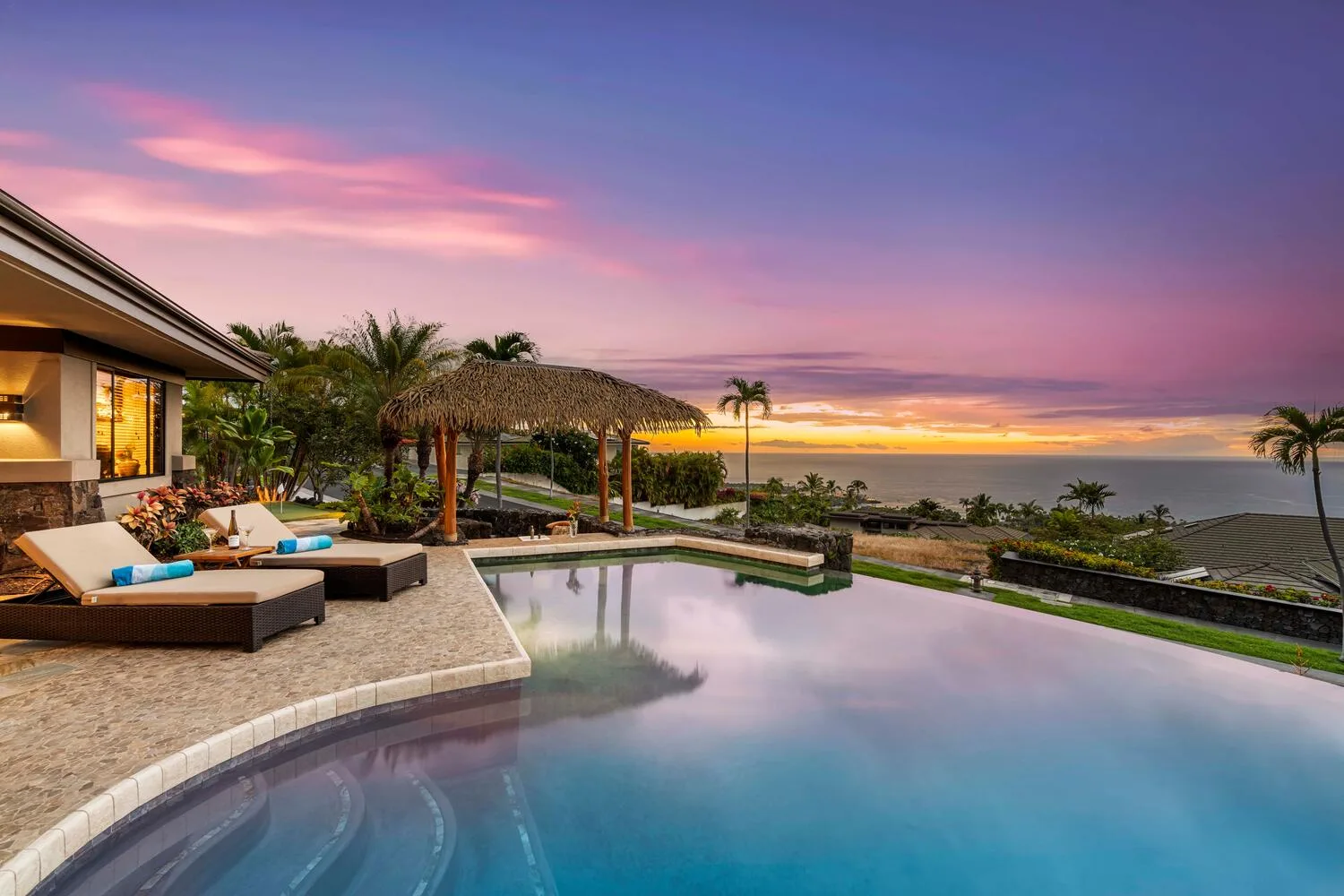 Una piscina al aire libre mira hacia el océano bajo un cielo colorido al atardecer.