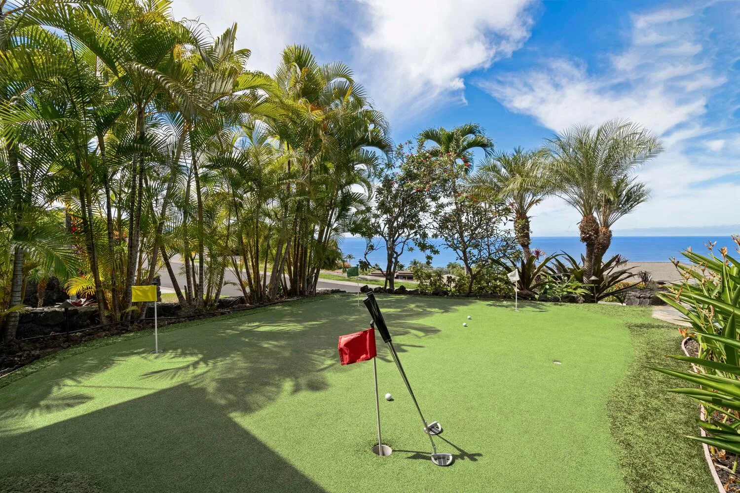 Campo de práctica de golf al aire libre, rodeado de palmeras y con el mar al fondo.