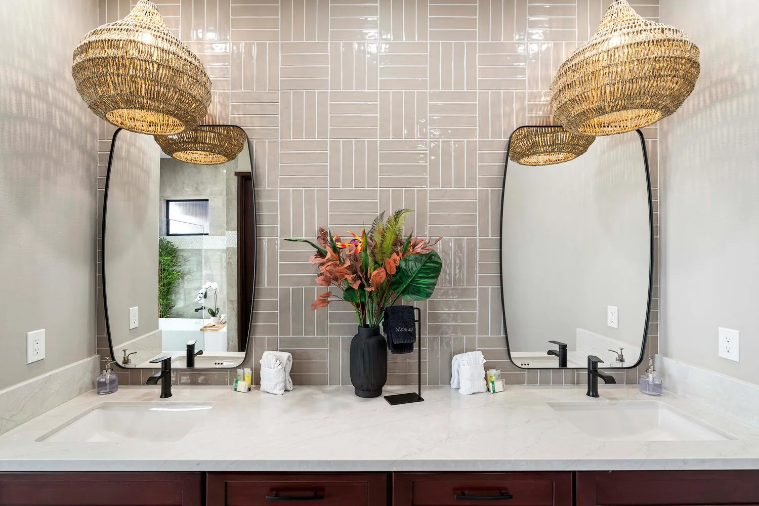 Un tocador de baño con dos lavabos, espejos altos y un arreglo floral.