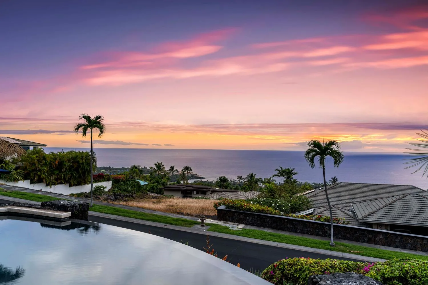 Paisaje costero al atardecer, con el océano detrás de un jardín y una piscina reflectante.