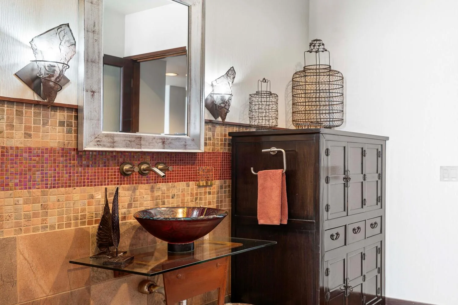 Un tocador de baño con lavabo de sobreponer, espejo de pared y salpicadero de azulejos.