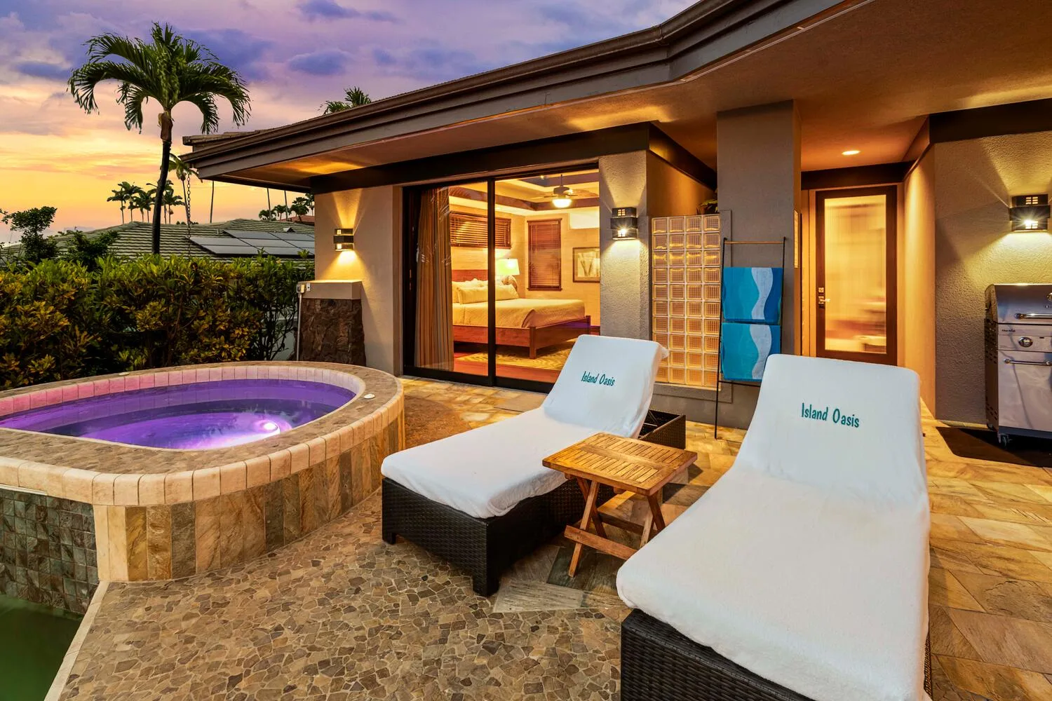 Un patio exterior con un spa circular y asientos acolchados junto a una habitación iluminada.