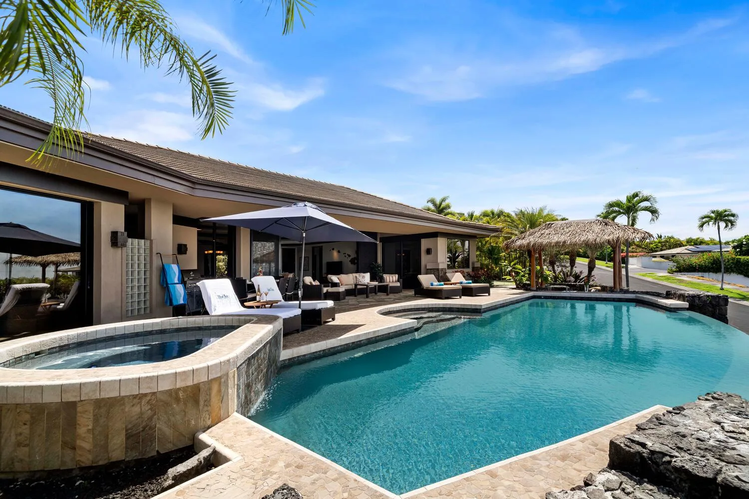 Una casa moderna da a una piscina con un spa circular elevado y asientos a la sombra.