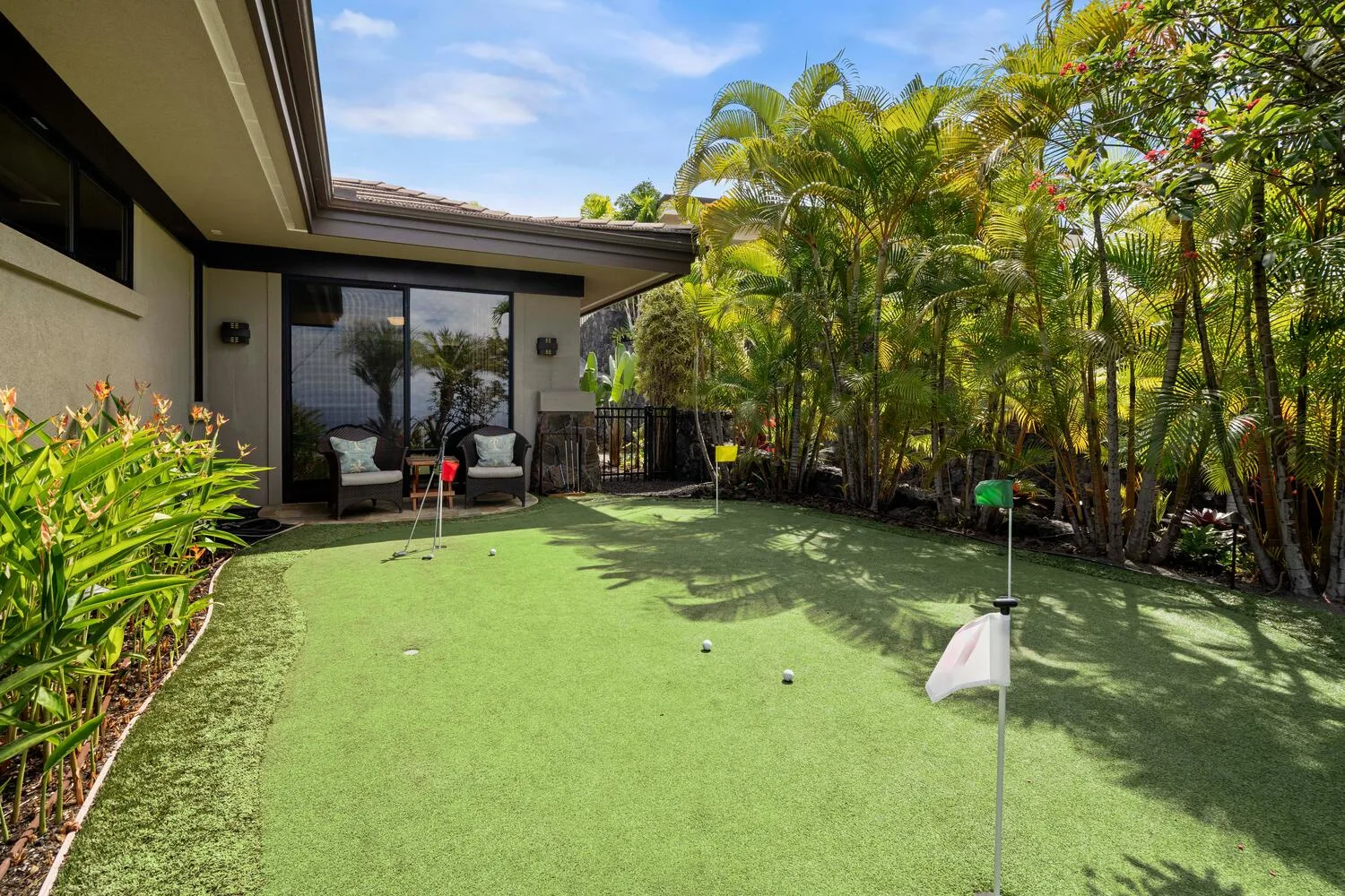 Un putting green junto a una casa, rodeado de plantas tropicales.