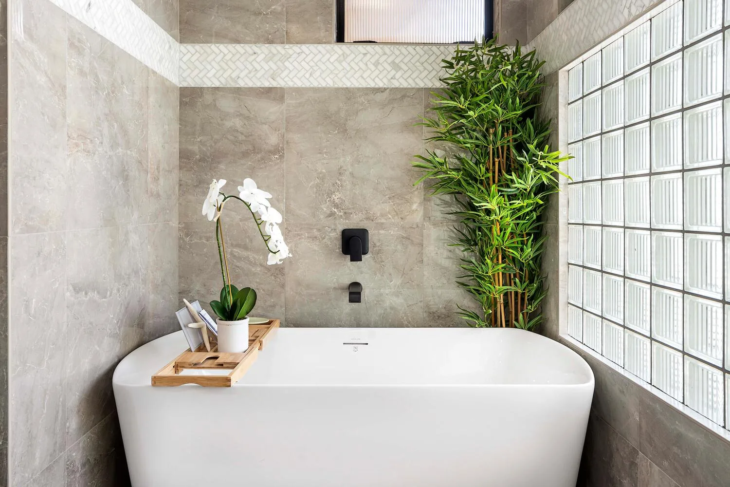 Un baño con una bañera exenta, una orquídea y una planta alta.