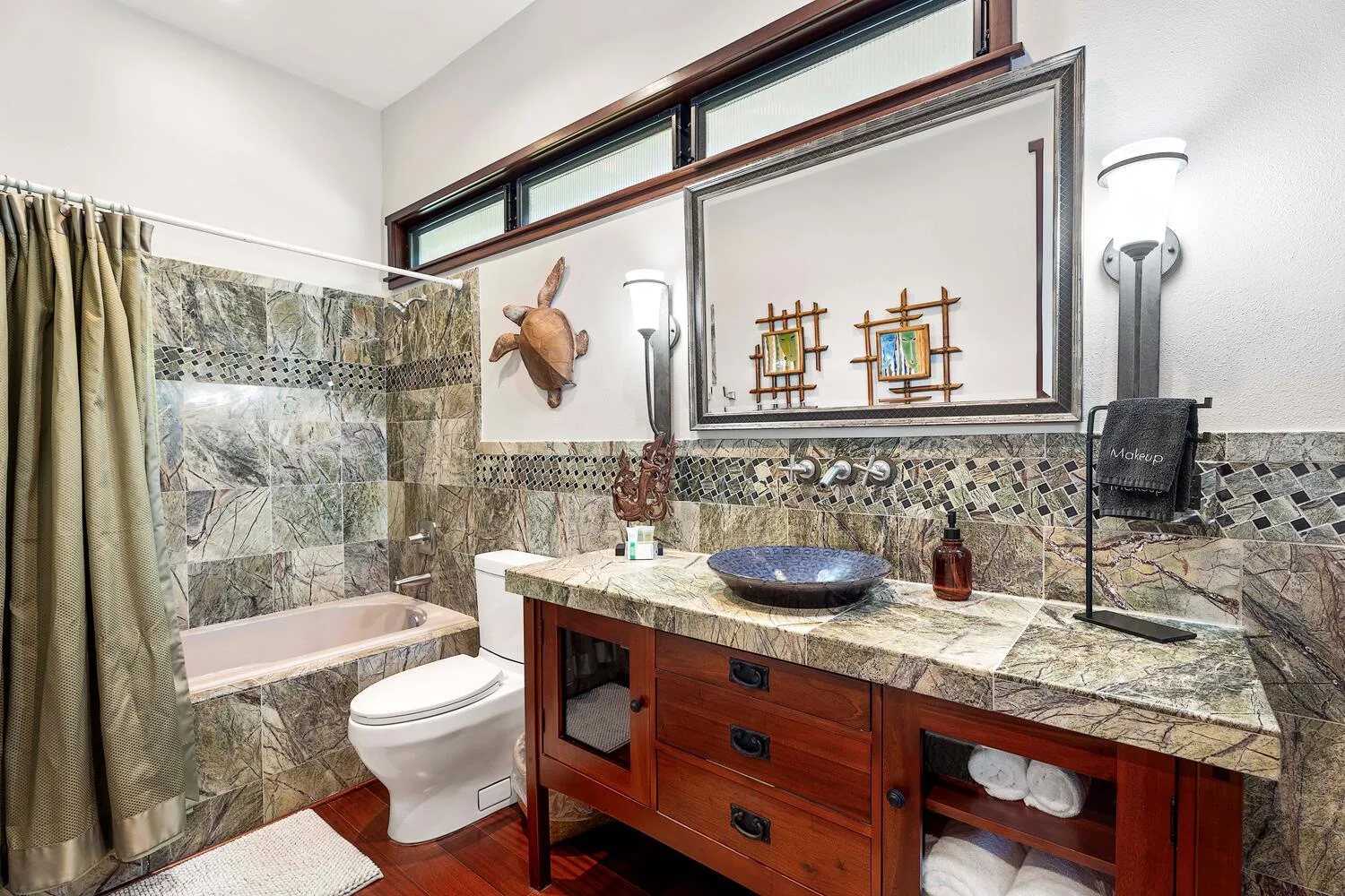 Un baño con ducha revestida de azulejos, inodoro y un amplio tocador con lavabo sobre encimera.