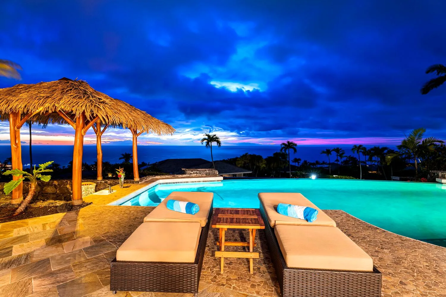 Un patio junto a la piscina al anochecer tiene dos tumbonas acolchadas.