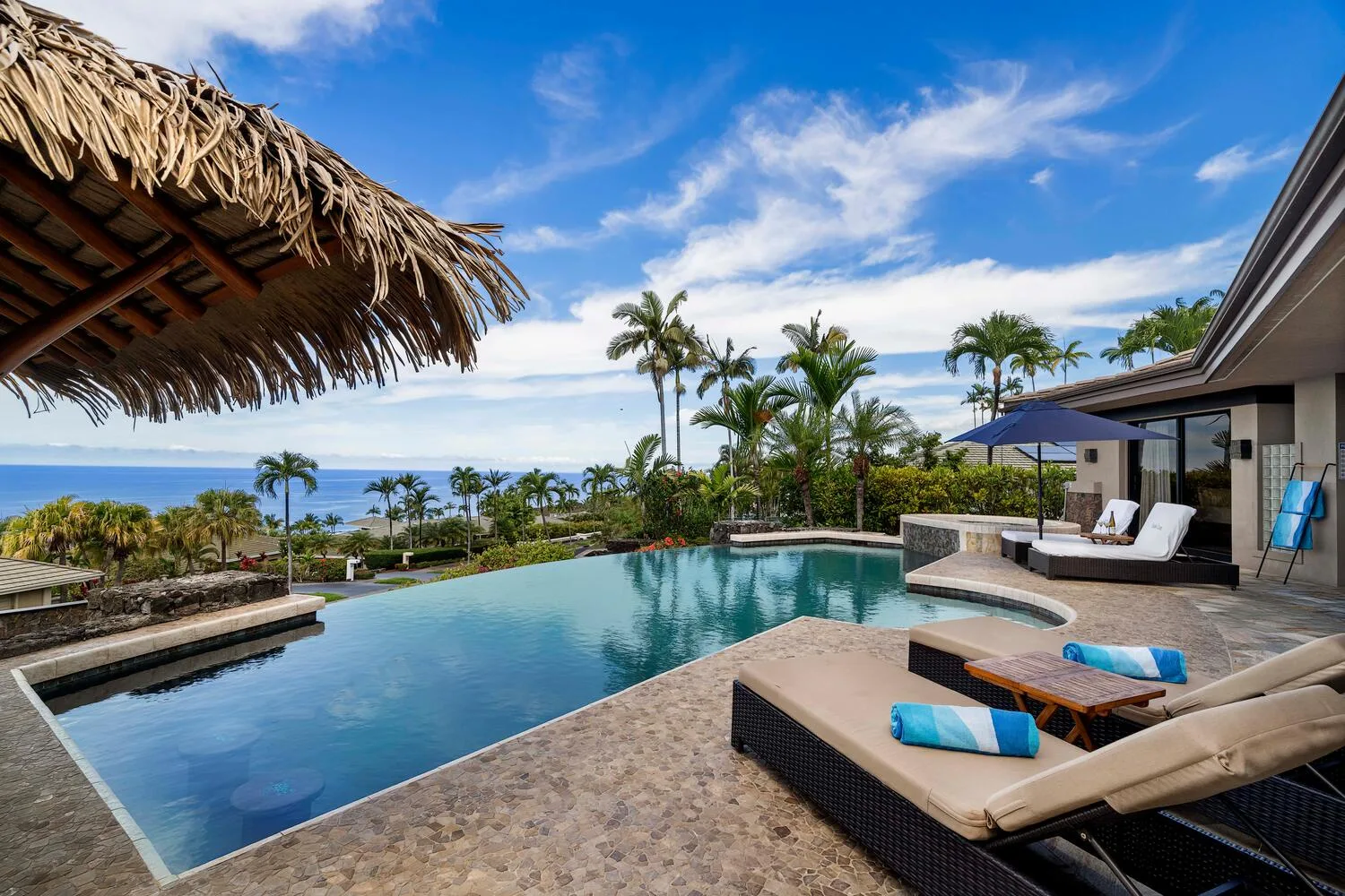 Una piscina tropical al aire libre mira hacia palmeras y el océano junto a una residencia moderna.