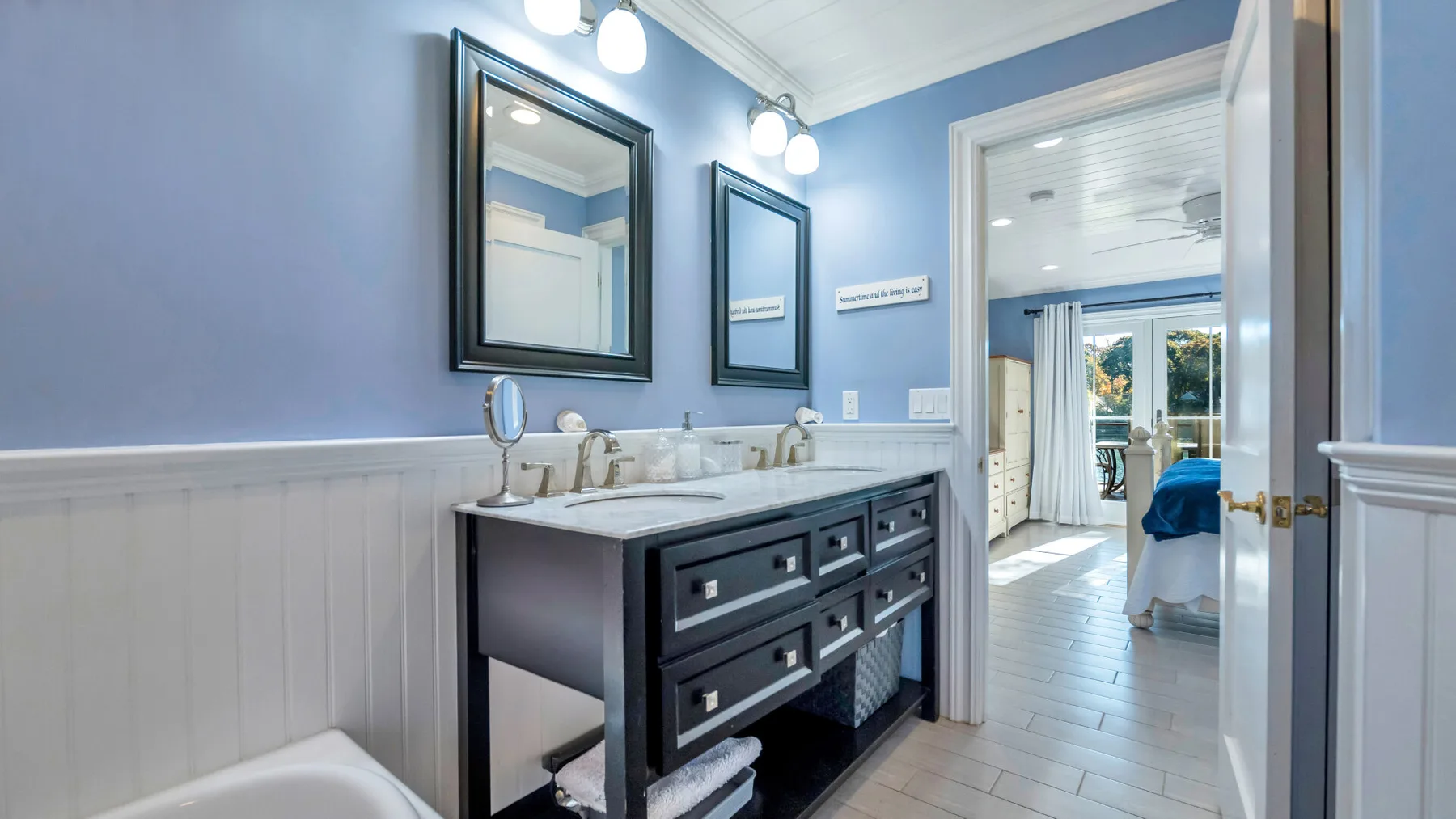 A bathroom vanity with a sink and mirrors, with a bedroom visible through the doorway.