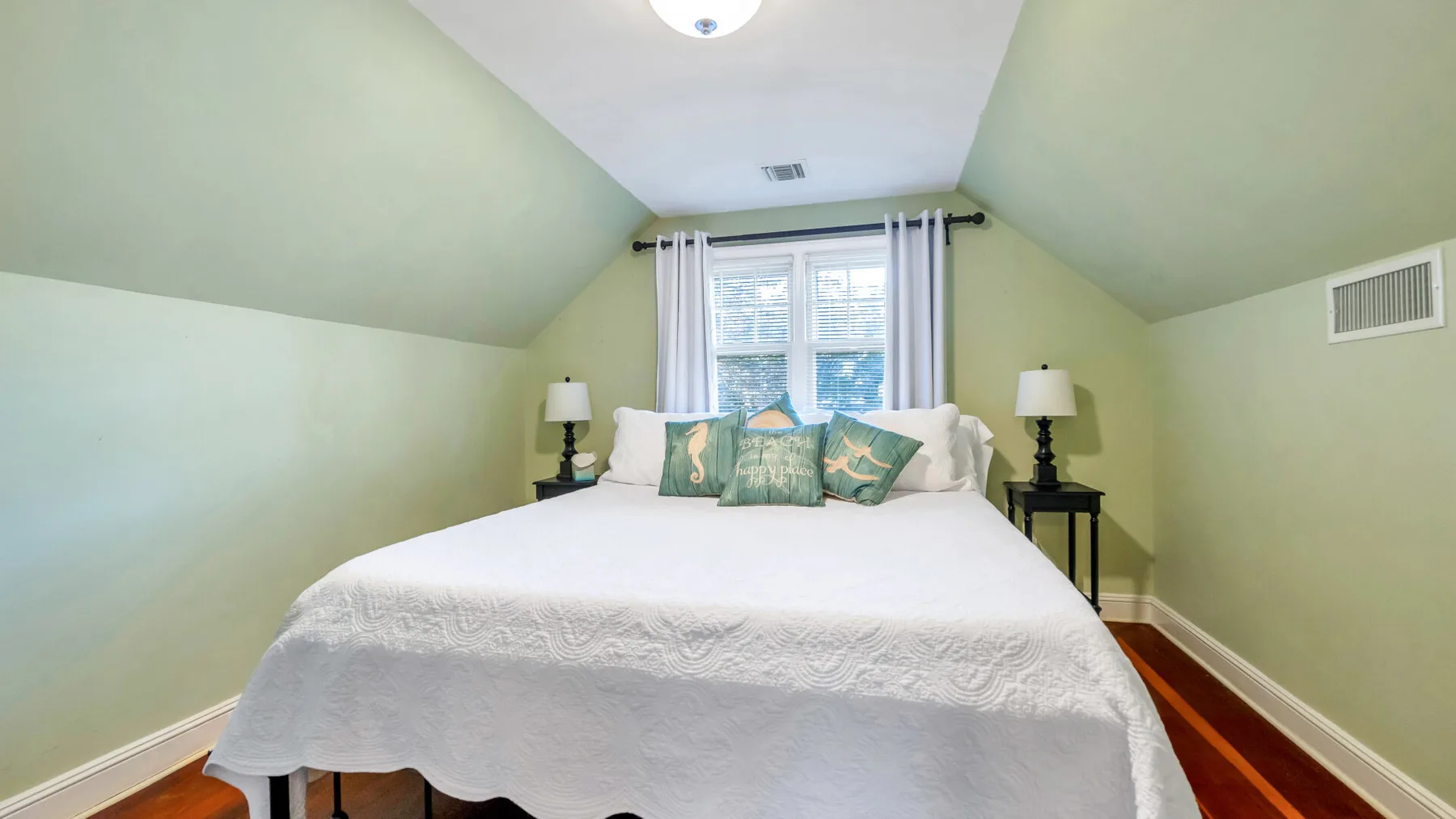 A bedroom with a bed beneath a window and light-colored walls.