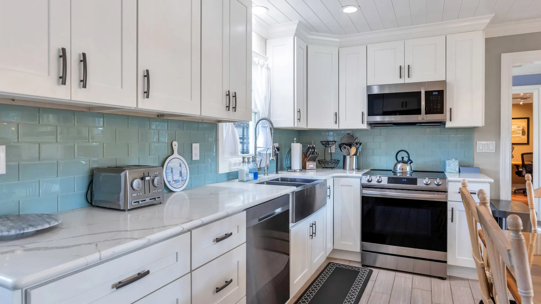 A bright kitchen with white cabinetry, blue tile, and stainless steel appliances.