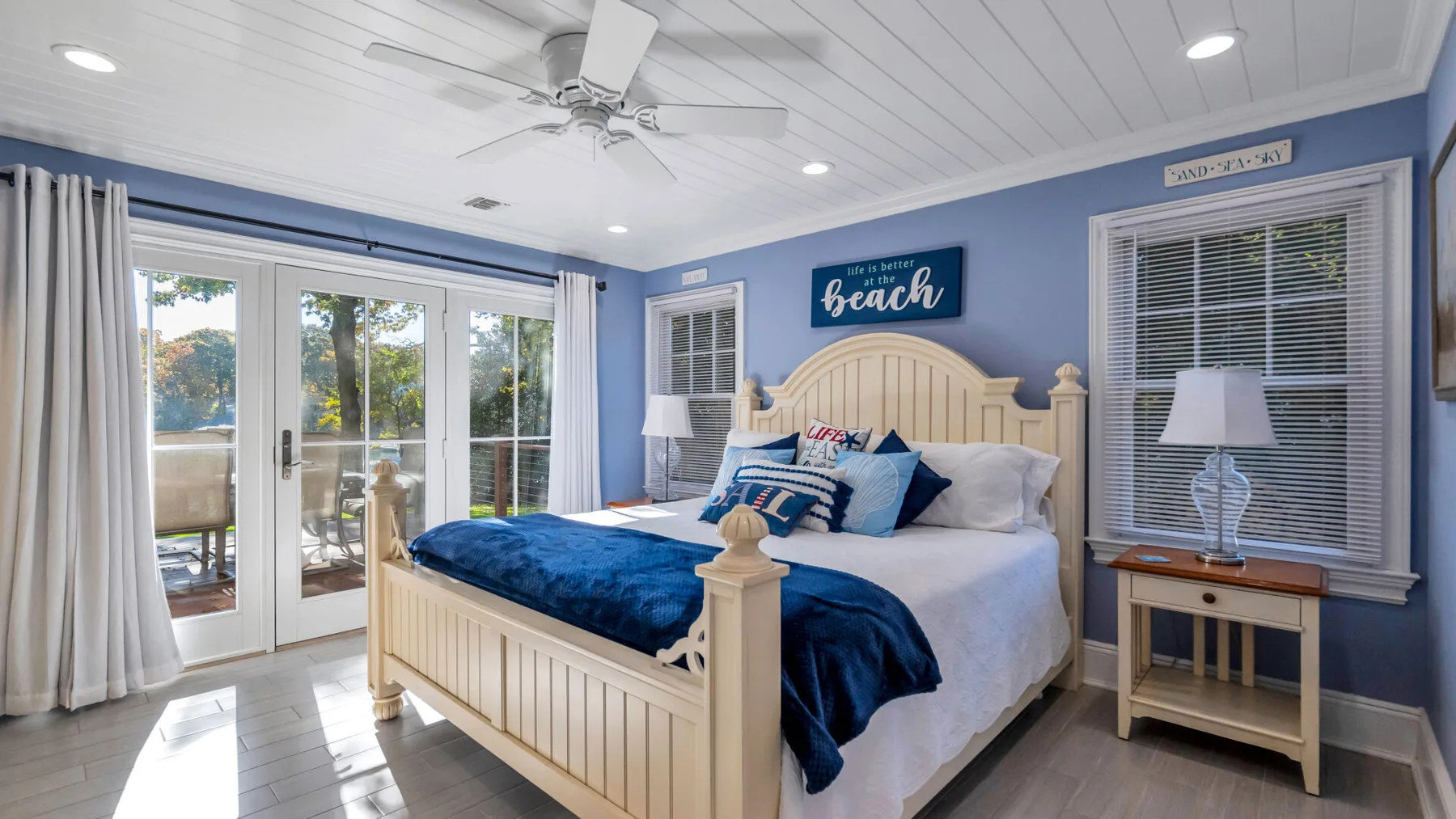 A bedroom with a light-colored bed, blue bedding, and glass doors opening onto a patio.