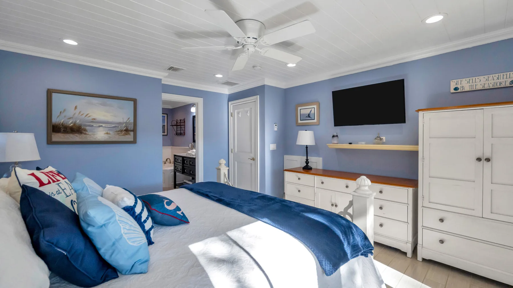 A blue bedroom features a bed with white bedding and a ceiling fan.