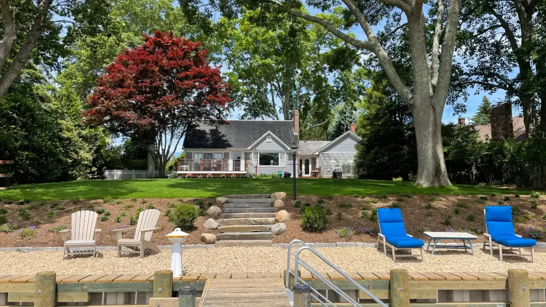 A landscaped yard with stone steps leads to a house, with seating on the lawn.