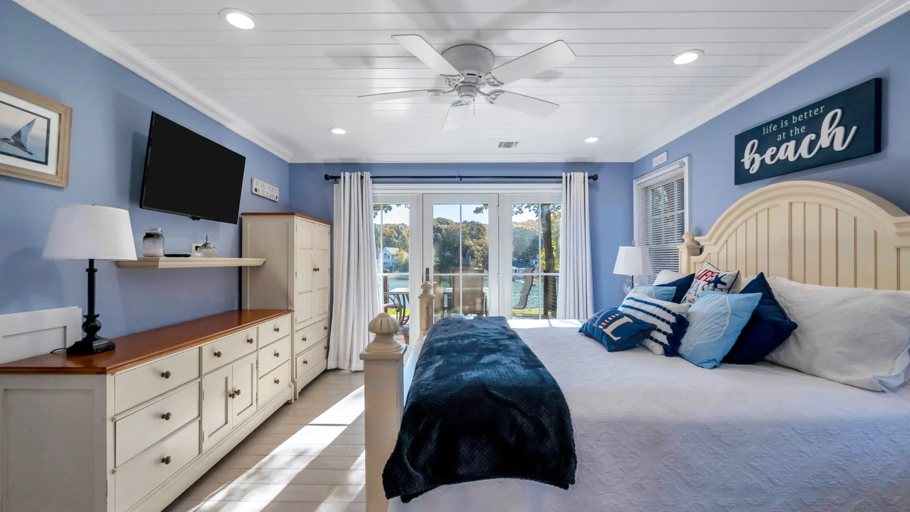 A bright bedroom with a large bed, blue bedding, and sliding glass doors.