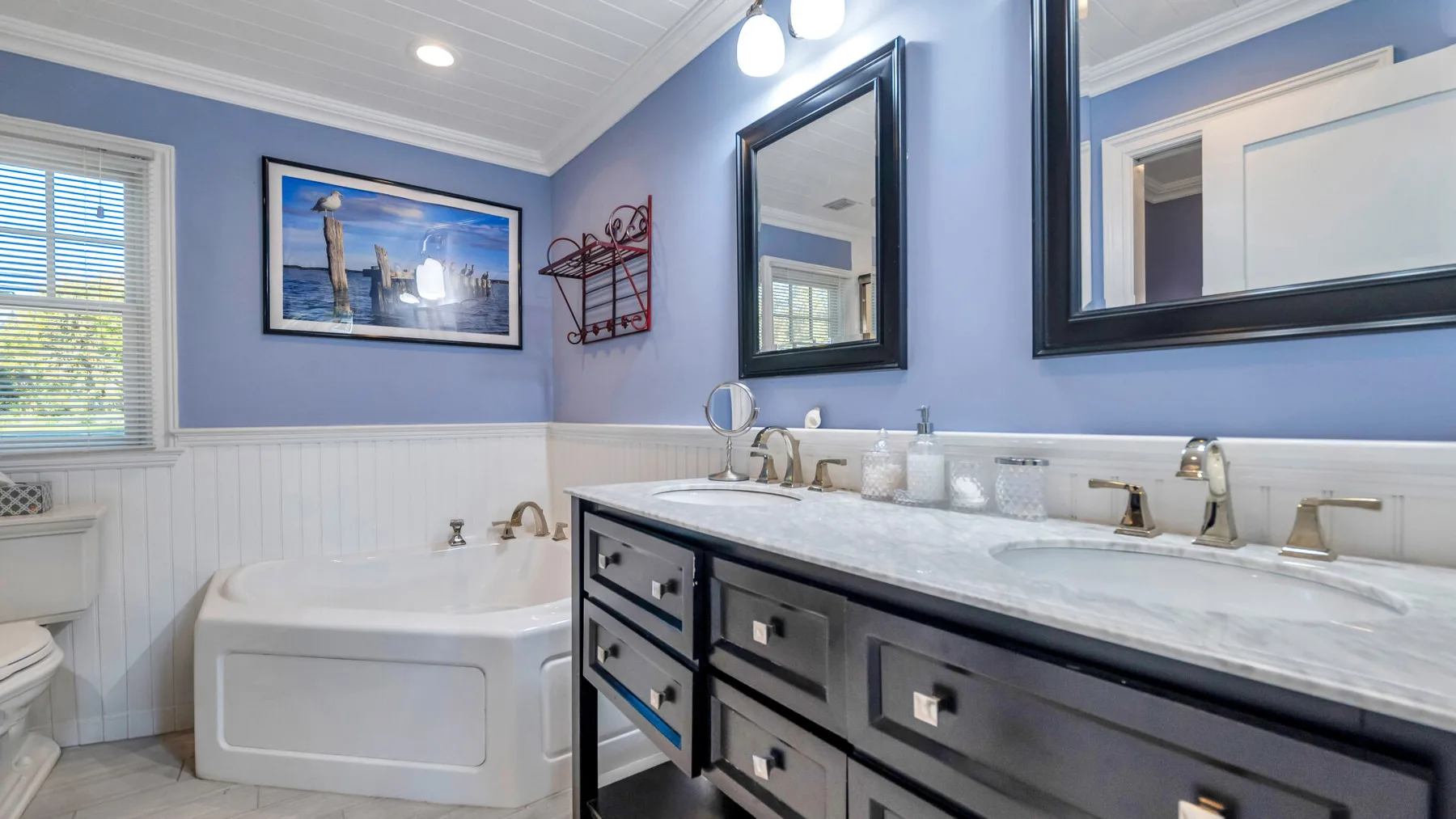 A bathroom with a bathtub, double sink vanity, and wall mirrors.