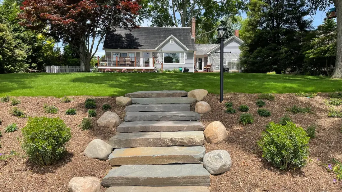 Stone steps lead up a landscaped lawn toward a house.