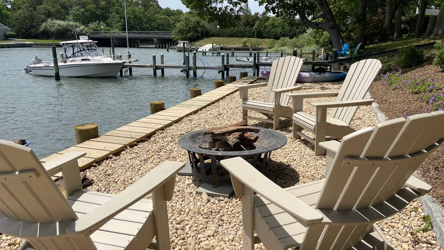 A pebble-covered waterfront patio has seating arranged around a fire pit.