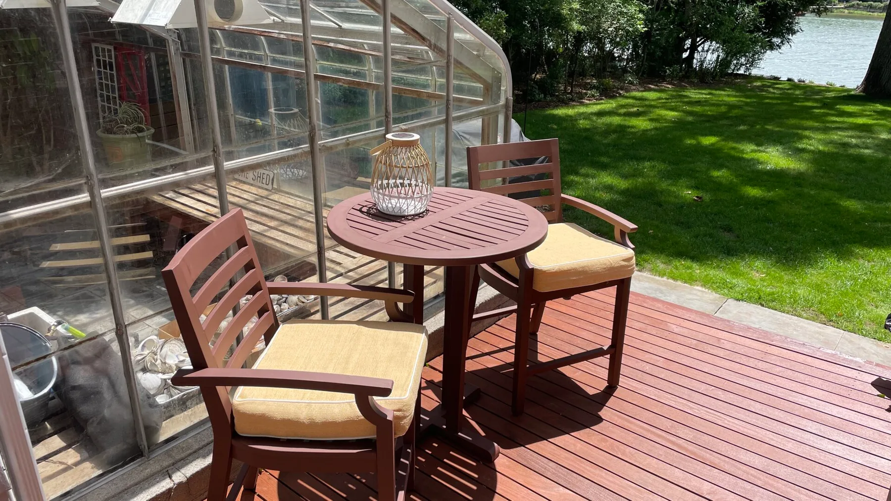 A small outdoor seating area on a wooden deck beside a glass sunroom.
