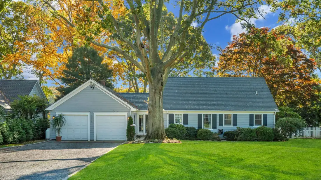 A single-story house with a large tree in the front yard.