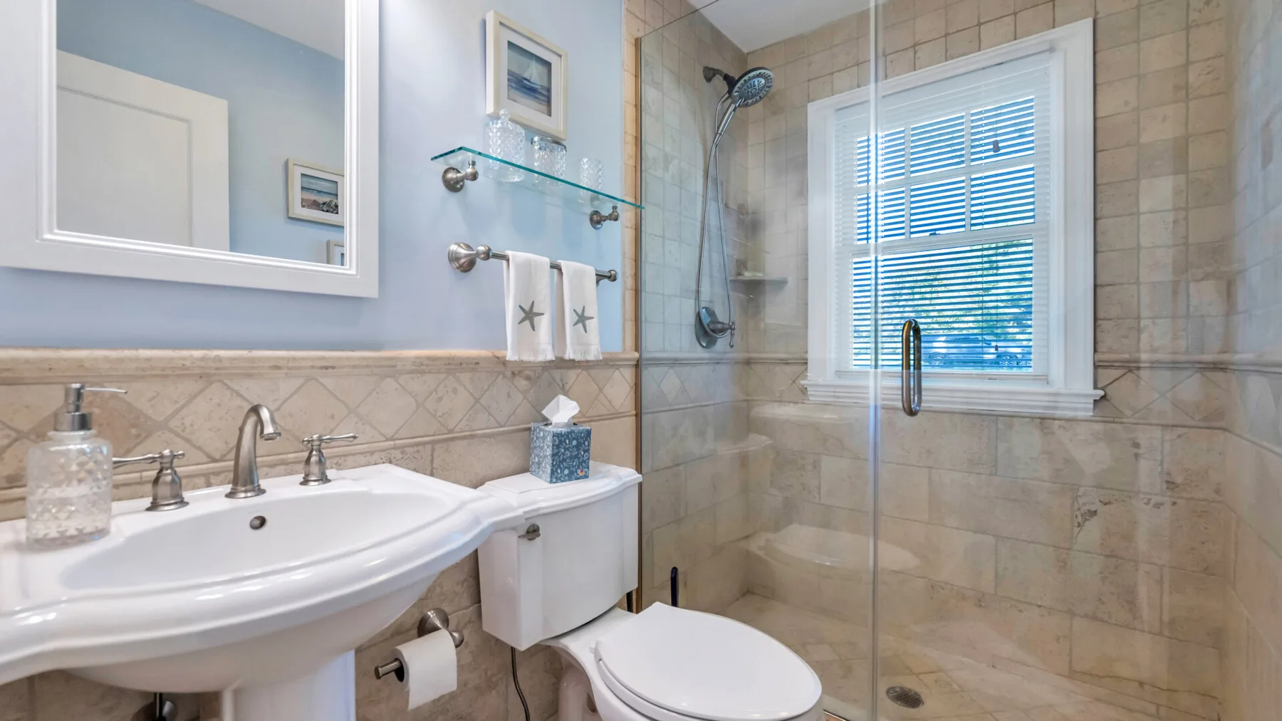 A bathroom with a sink, toilet, and glass shower beside a window.