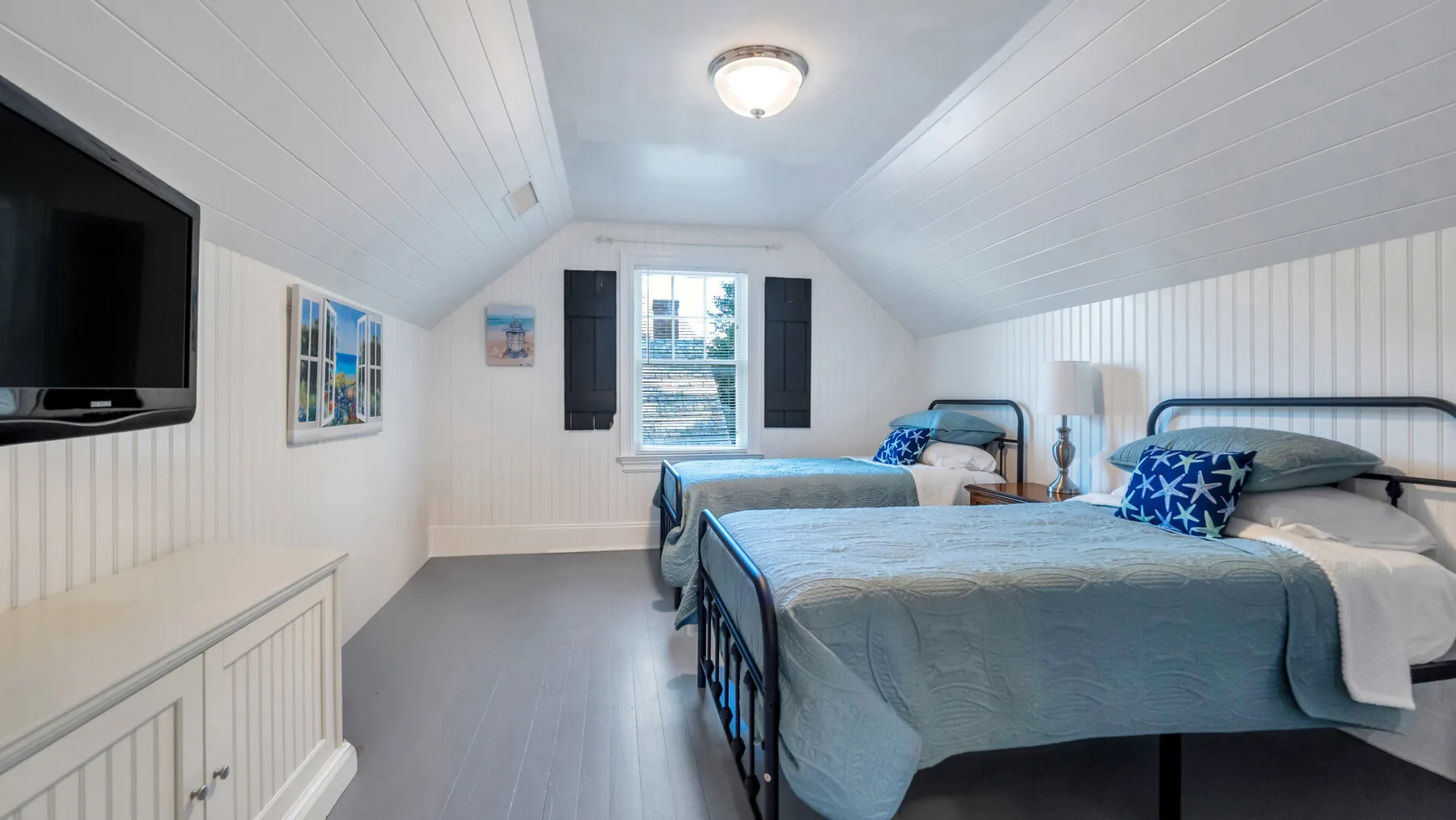 A bright bedroom with two beds and a window beneath a sloped ceiling.