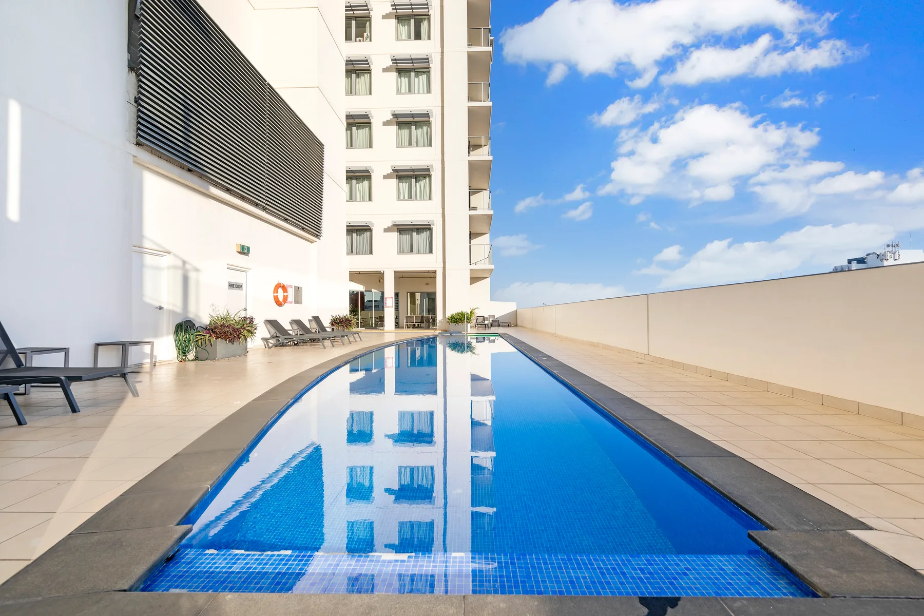 Una piscina en la azotea junto a un edificio alto, con asientos junto a la terraza.