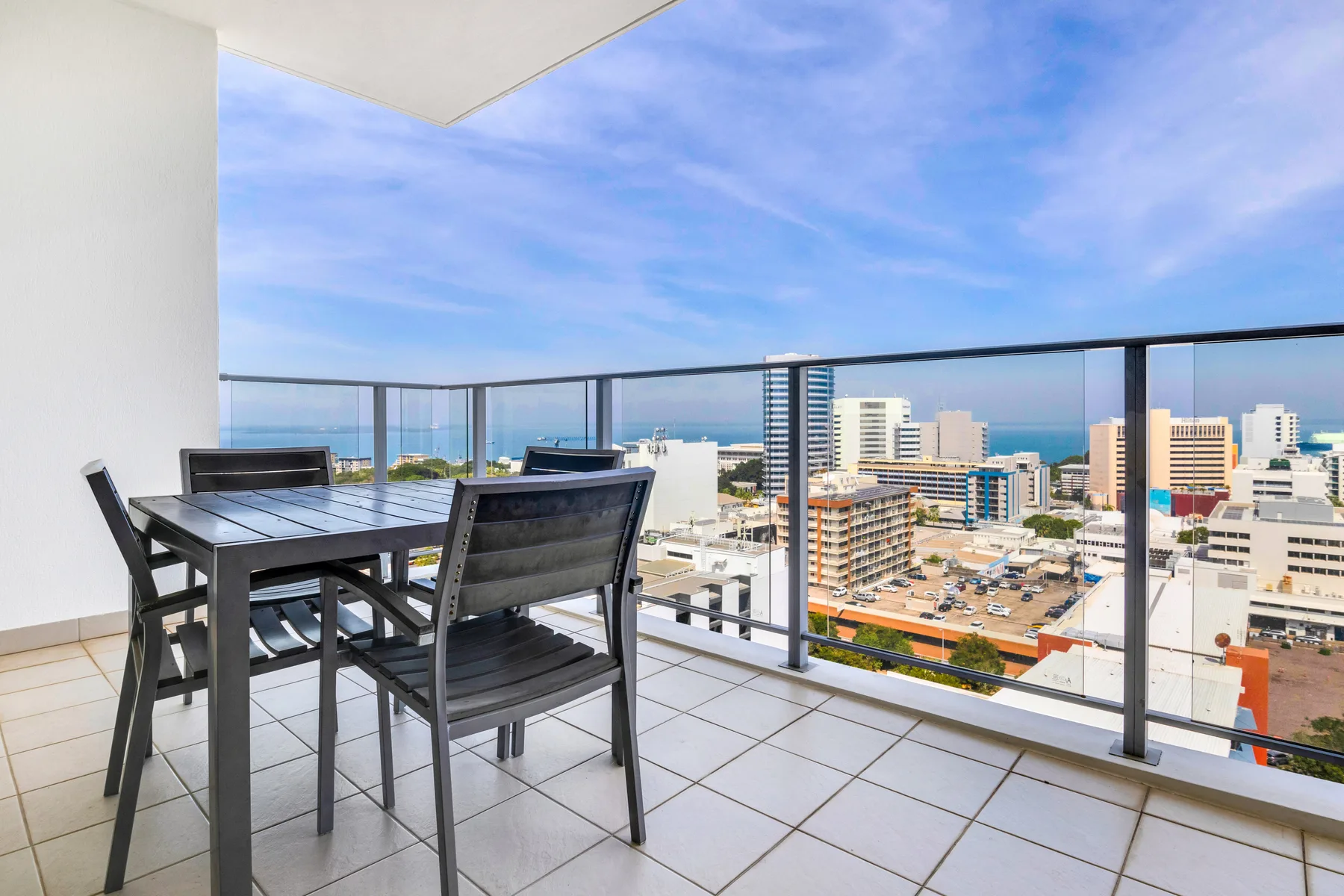 Una zona de comedor en un balcón tiene vistas a edificios de la ciudad y al mar.