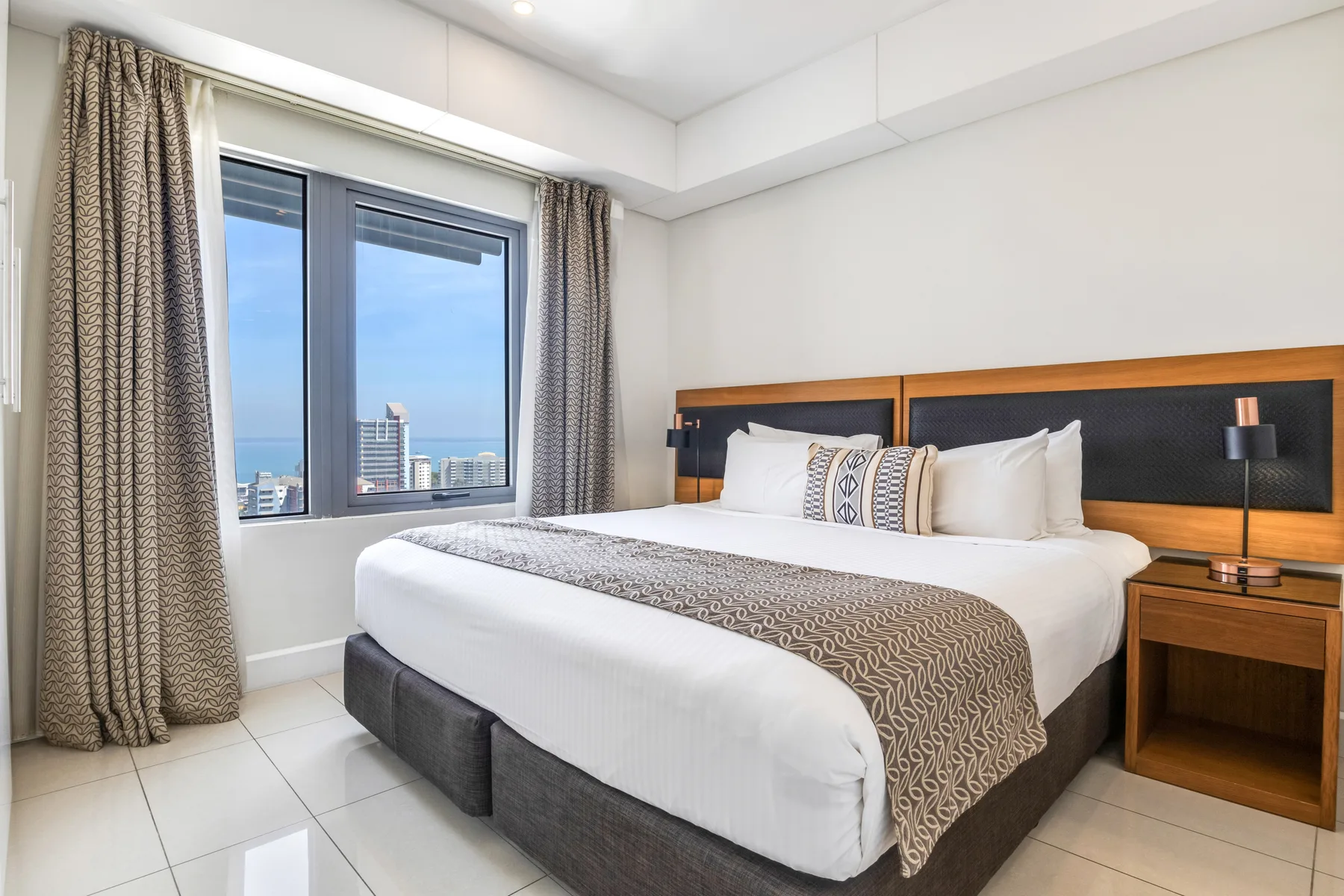 Un dormitorio con una cama grande y cortinas que enmarcan una ventana con vistas al agua.