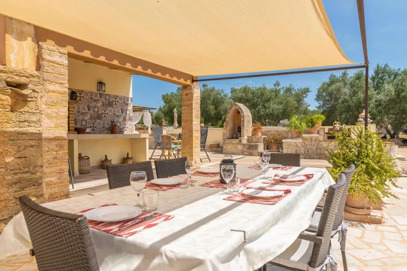 Una zona de comedor al aire libre está bajo un gran toldo, con una mesa larga preparada para comer.