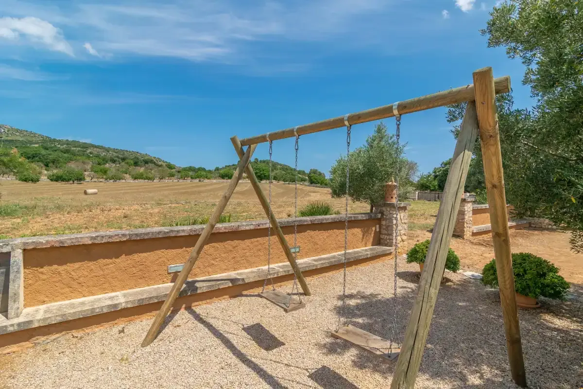Un columpio de madera está junto a un muro bajo en un patio seco.